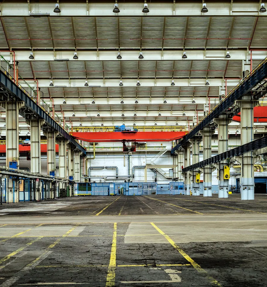 Steel-framed industrial hall with overhead crane rails and high-bay lighting.